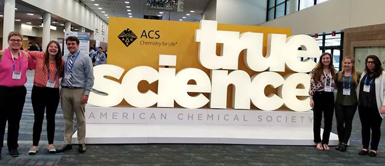 Students standing by the ACS Sign that reads "True Science"