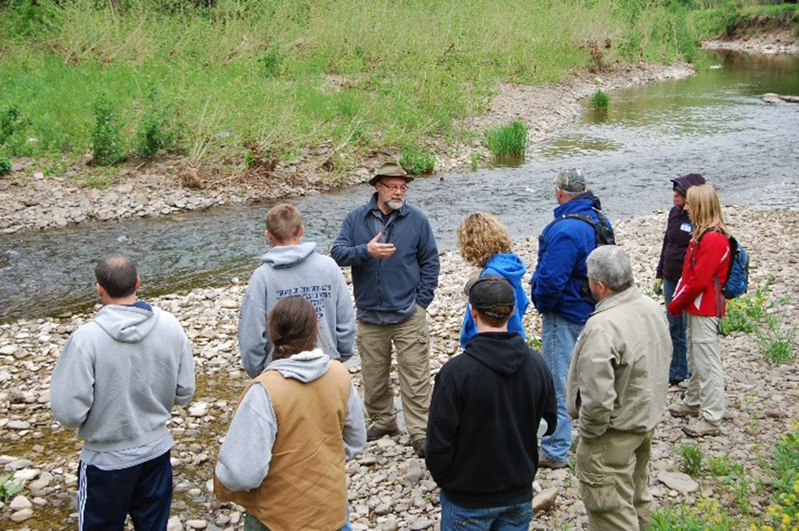 Professor presenting to a group of students while standing on a river bank
