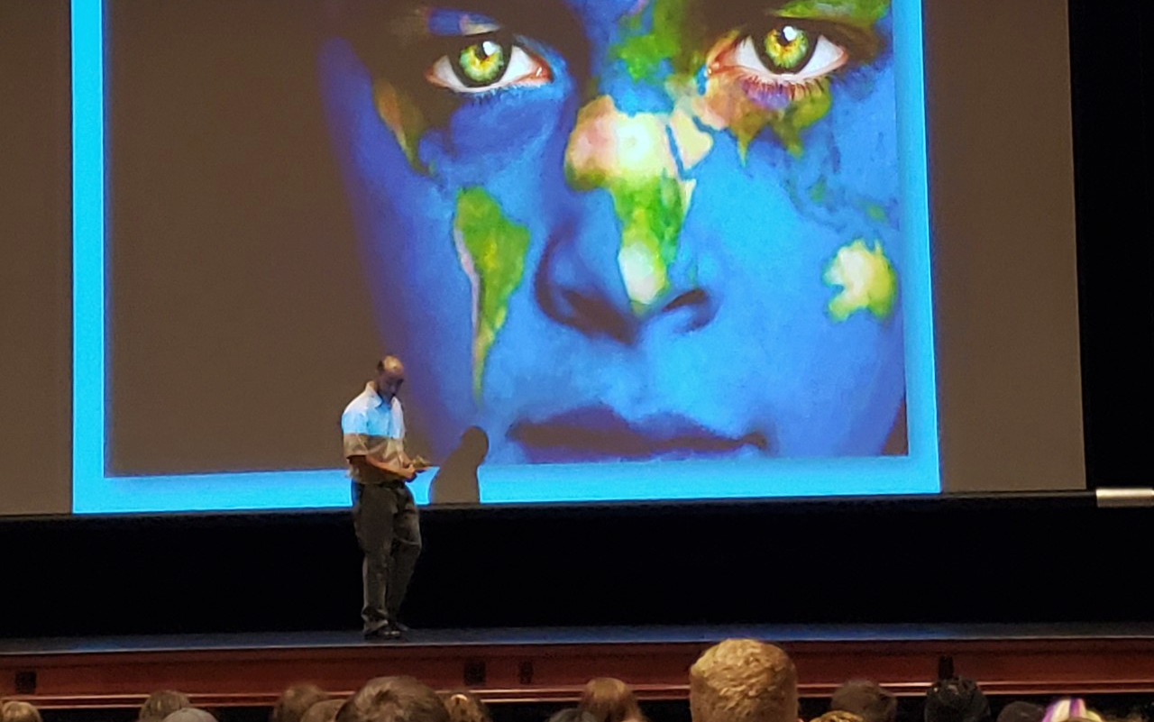 Multicultural Affairs presentation event in auditorium, picture of face with Earth on the projector