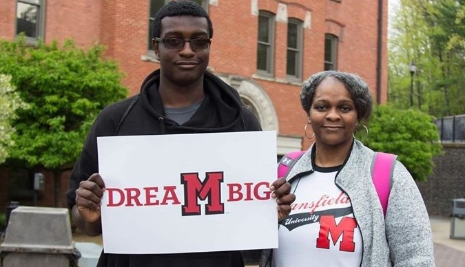An MU student standing next to his friend and holding a sign reading Dream Big